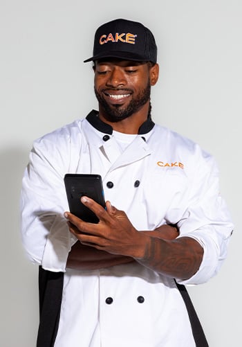 A man in a chef's uniform smiles while using a CAKEpop handheld POS.