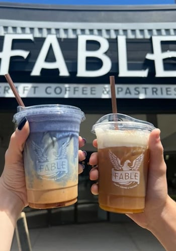 Two customers holding coffee drinks with the Fable Coffee logo visible on the cups.