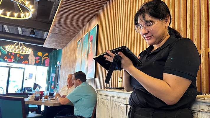 A woman who works at a Mexican restaurant uses a CAKE mobile POS device to take an order from a customer.