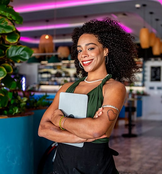 A smiling woman holding a clipboard in a restaurant, representing a manager's role in daily operations.