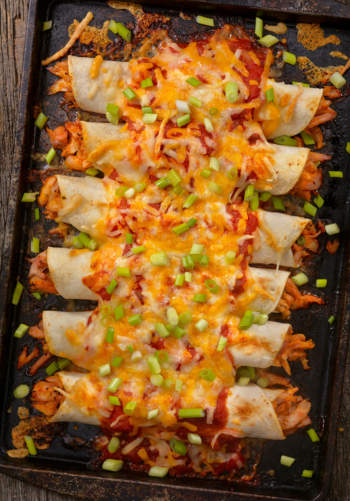 A tray of baked or fried flautas topped with cheese and sauce.