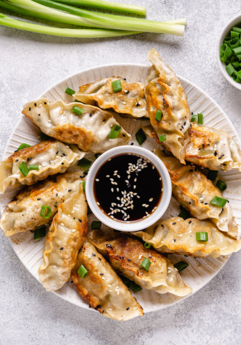 A plate of pan-fried gyoza with a side of dipping sauce.