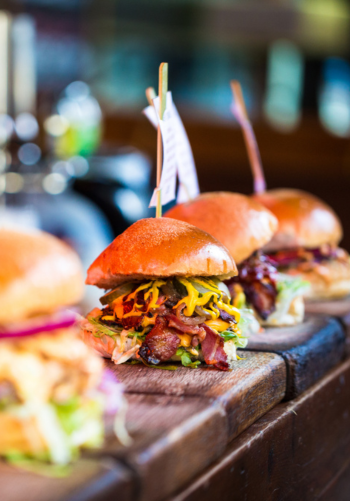 Two gourmet burgers on a wooden board with a side of french fries.