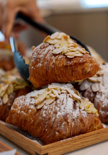 A close-up of a hand holding a freshly baked, flaky almond croissant.