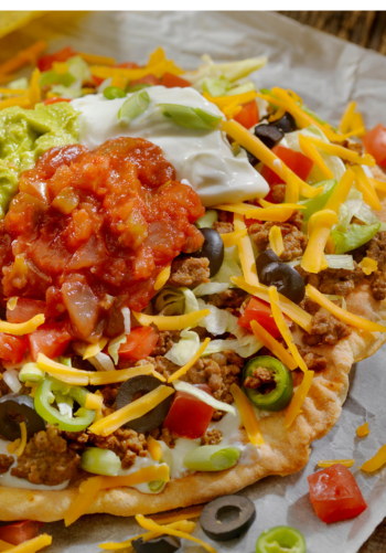 A large plate of loaded nachos with ground beef, cheese, and salsa.