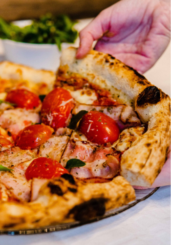 A hand serving a slice of fresh pizza topped with tomatoes and basil.