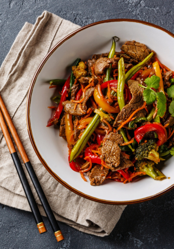 A bowl of beef and broccoli stir-fry served with chopsticks.