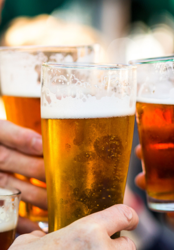 Two beer glasses being held up in a toast at a bar.