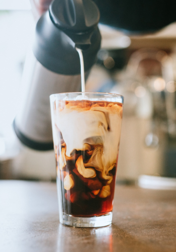 Milk being poured into a glass of iced coffee to create a marbled effect.