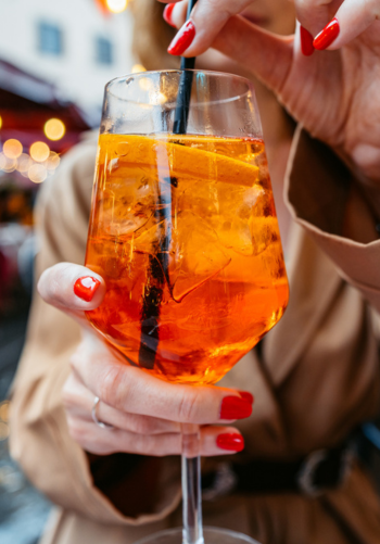 A close-up of a hand holding a vibrant orange cocktail with a straw.