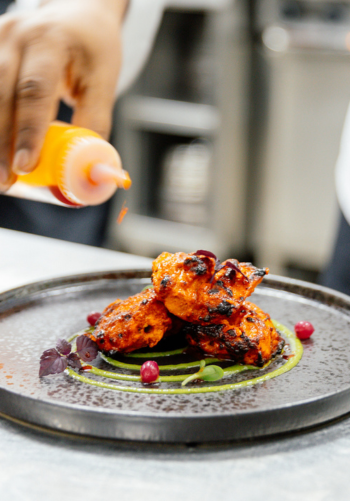 A platter of tandoori chicken garnished with cilantro and served with a dipping sauce.