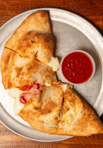A golden-brown calzone sliced open to reveal the inside, served with a side of marinara sauce.