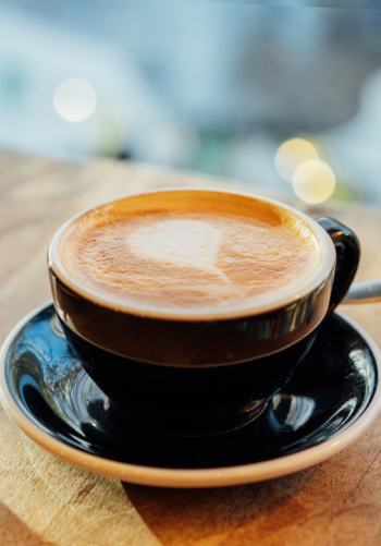 A close-up of a cup of hot latte with intricate latte art on a wooden surface.