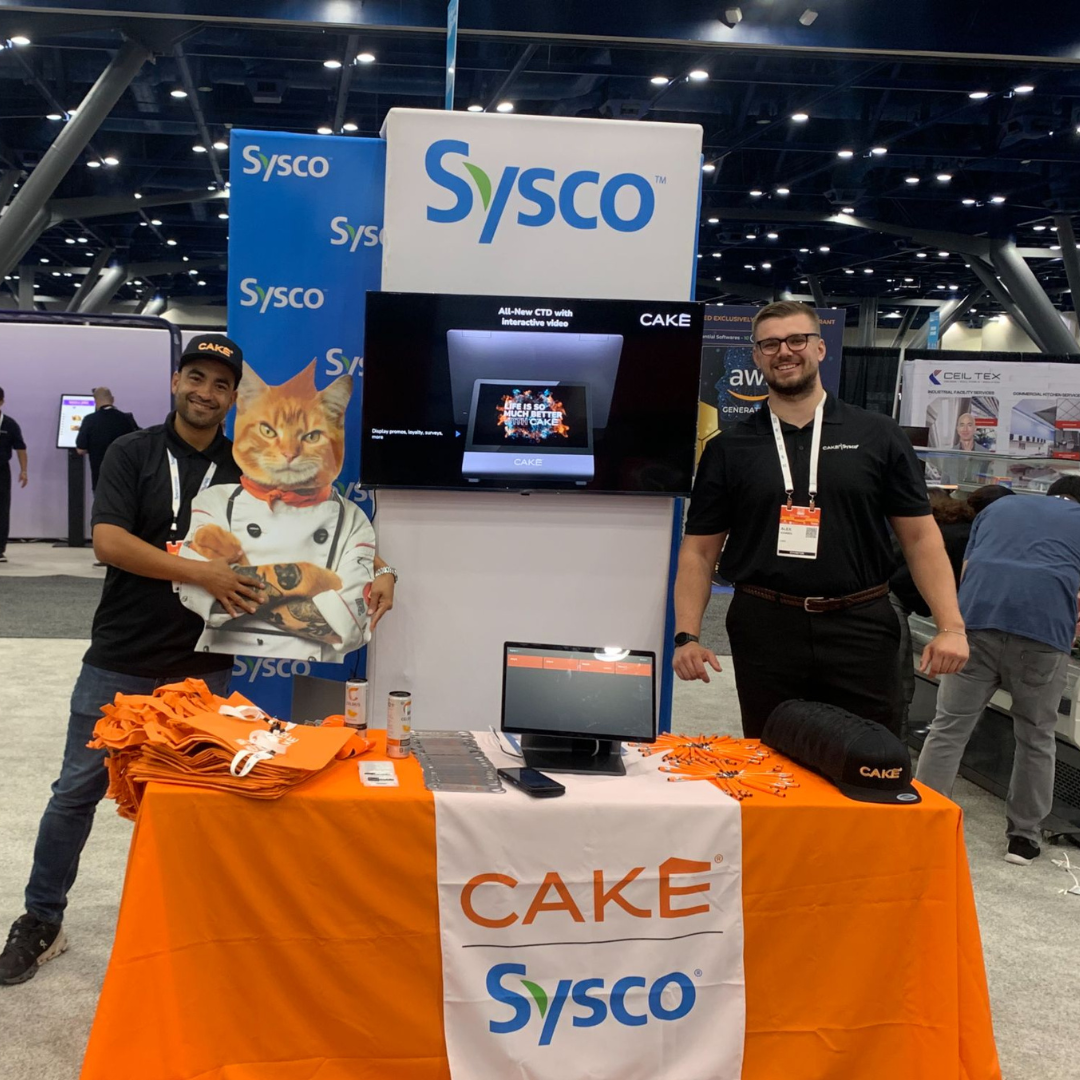 A CAKE employee and a Sysco representative smiling together at a CAKE booth at a local event.