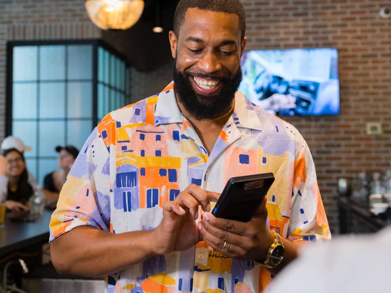 A restaurant staff member smiles while holding the CAKEpop handheld POS, highlighting fast service.