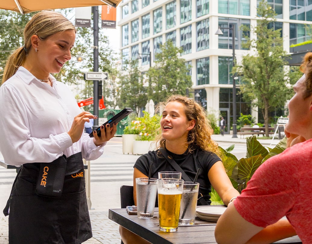 A woman smiles while using the CAKEpop handheld POS to serve customers.