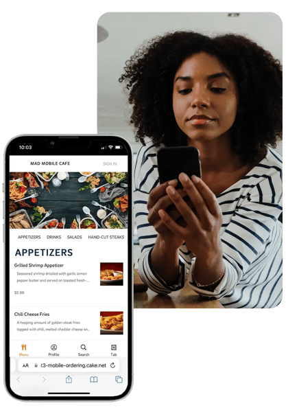 A woman smiles as she looks at her smartphone, which shows a CAKE online ordering menu, with a larger screen behind her displaying the same menu.
